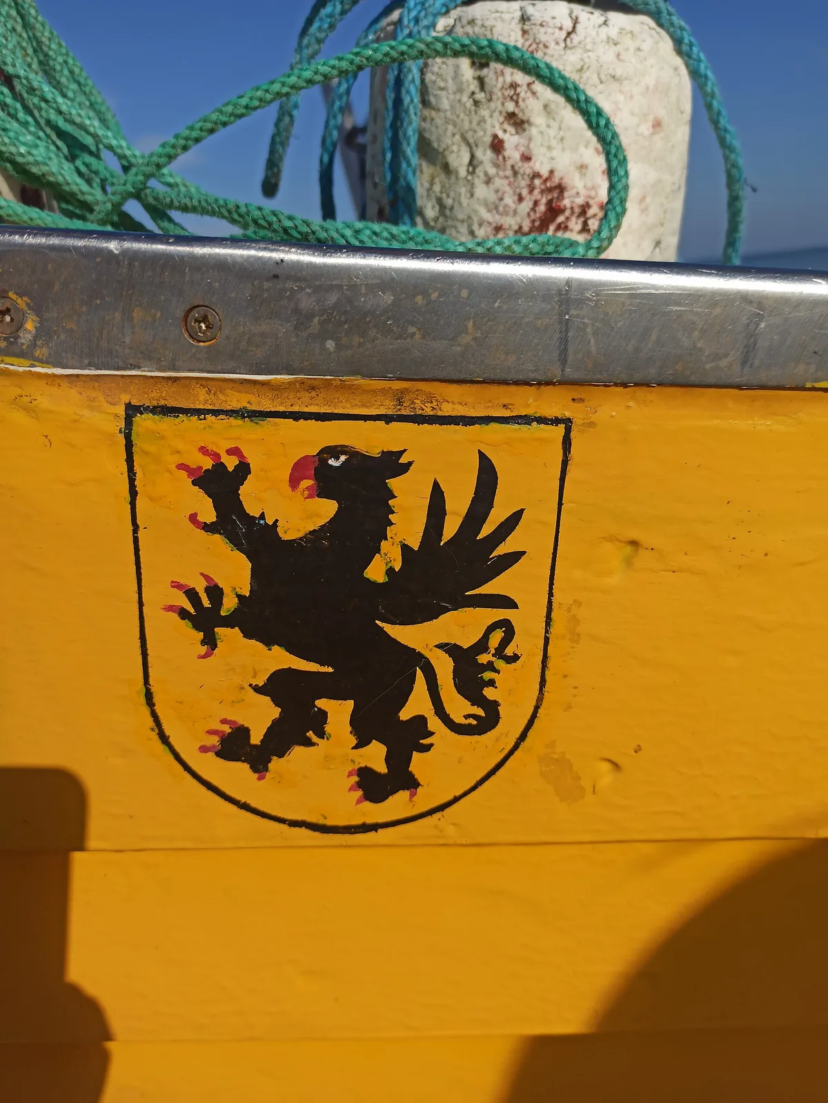 Żółta burta drewnianej łodzi rybackiej, na niej namalowana tarcza z czarnym gryfem.
